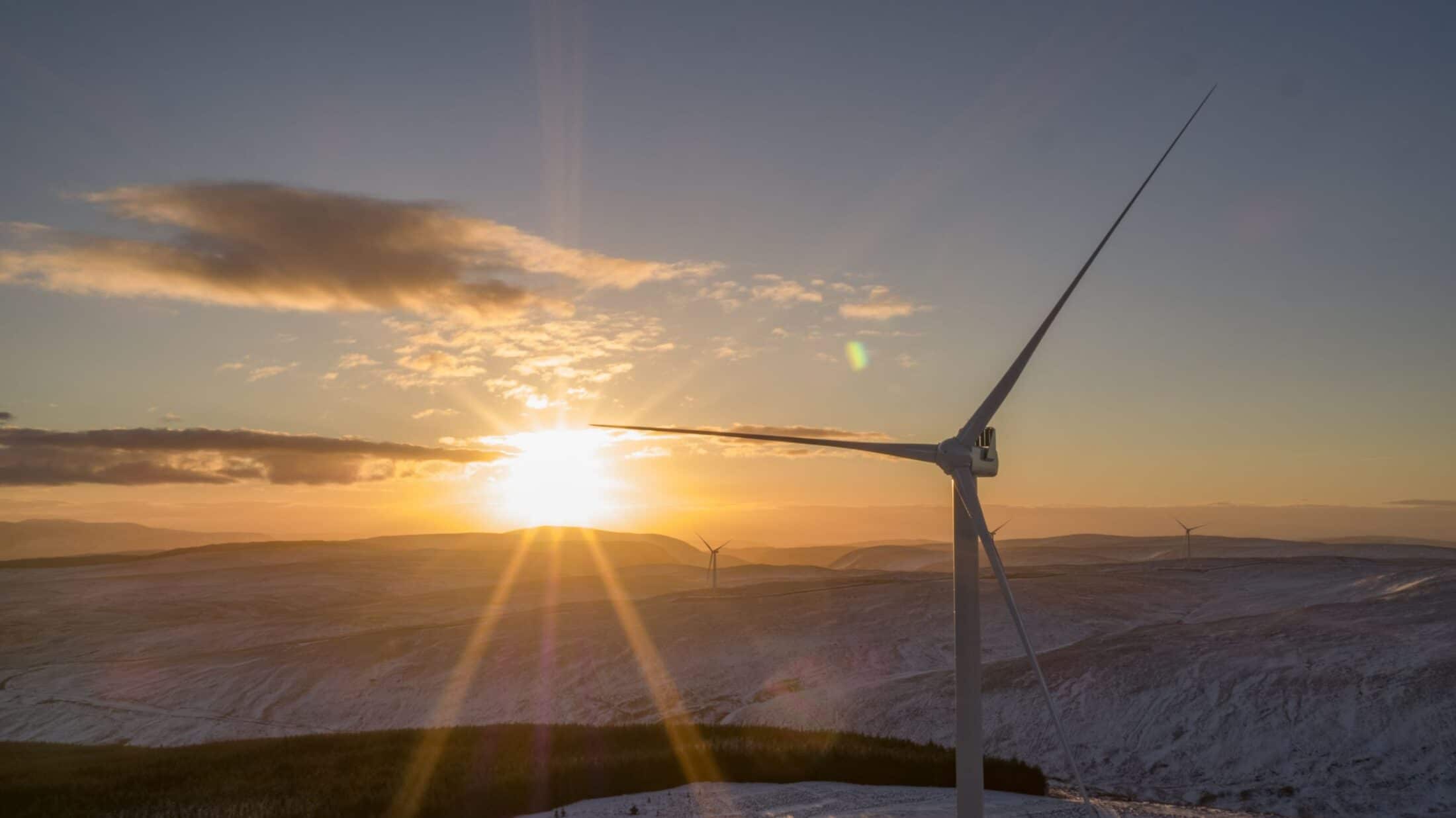 Wind turbine silhouetted against a sunrise over snow-covered hills