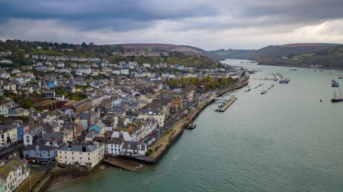 Drone filming featuring Dartmouth Harbour. Fishing boats in the water and the Naval College on the hill. Shops and Houses on the hill.