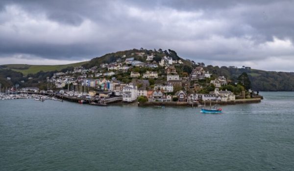 Dartmouth Harbour with boats and houses on a hill. The sea is in the foreground with dark skies.