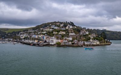 Dartmouth Harbour with boats and houses on a hill. The sea is in the foreground with dark skies.
